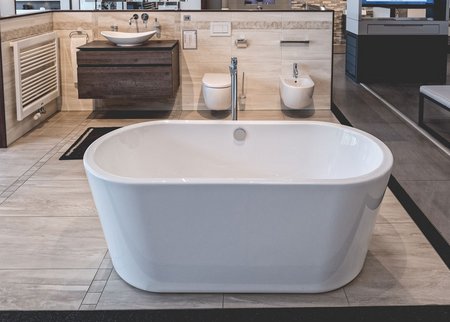 Moderne Badausstellung mit freistehender Badewanne, wandhängendem Waschtisch, Bidet, WC und großformatigen Wandfliesen.