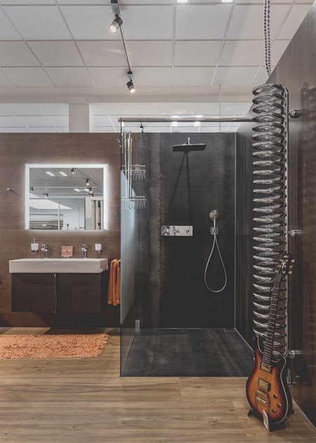 Moderne Ausstellung mit offener Dusche in dunklen Fliesen, doppeltem Waschtisch, orangefarbenen Handtüchern und dekorativer Gitarre.