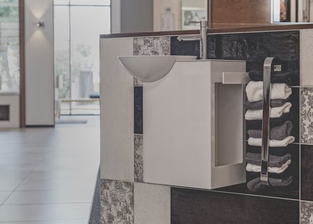 Weißer Waschplatz mit runder Aufsatzschale und modernem Armaturendesign, ergänzt durch strukturierte Wandfliesen und ordentlich gestapelte Handtücher.